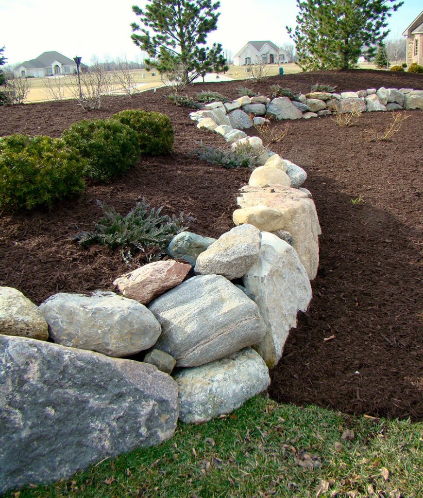 A rock retaining wall curves through a garden yard